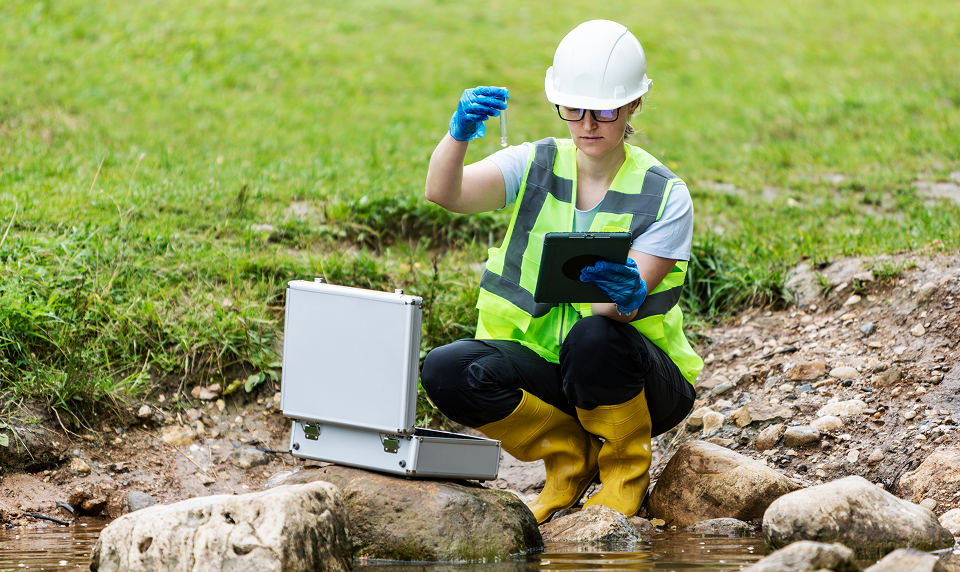 Scientist testing water by a stream.
