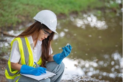 A woman in hard hat writing on paper near water.