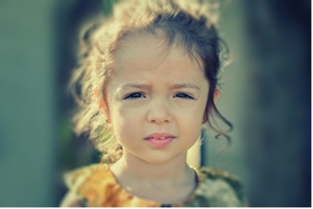 A young girl with her eyes closed and looking at the camera.